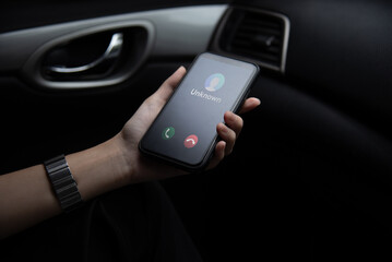 Hand holding a smartphone displaying an unknown caller ID Scam, fraud or phishing with smartphone inside a vehicle.