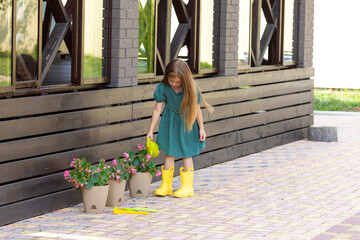 Adorable little girl is watering flowers in pots in garden outside house, child education of...