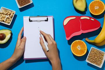 Paper mockup of liver, food and folder in hands on blue background, top view