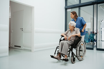 Portrait of nurse pushing senior patient in wheelchair across hospital corridor. Emotional support...
