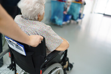Close up of nurse pushing senior patient in wheelchair across hospital corridor. Emotional support...