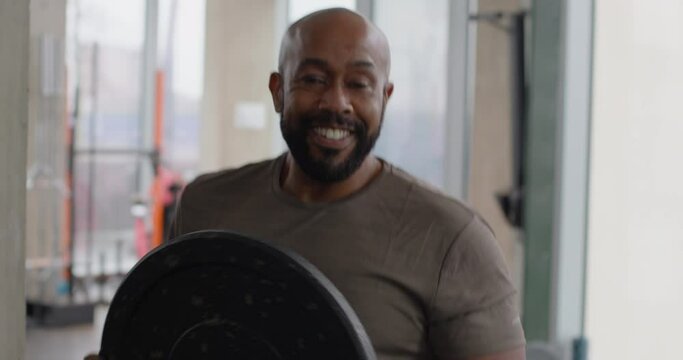 Male Lifting Barbell Weight and Looking into Camera Smiling