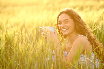 Happy woman drinking coffee looking at you in a field