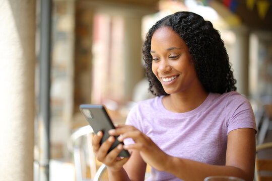 Happy black woman is using phone in a restaurant