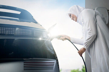 Asian muslim woman charging her EV at home shot from low angle