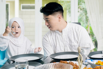 Father talking to his cute daughter wearing hijab at dining table