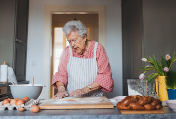 Senior woman preparing traditional easter meals for family, kneading dough for easter cross buns....