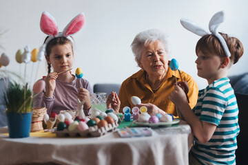 Grandmother with little kids decorating easter eggs at home. Tradition of painting eggs with brush...