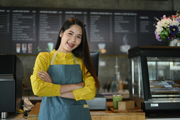 Portrait of confident small coffee shop owner standing with arms crossed at counter