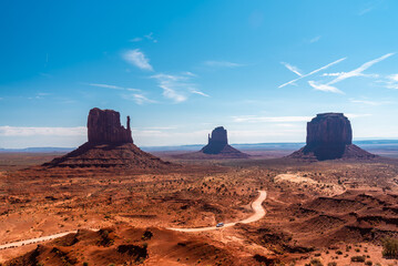 Dirt road winding through Monument Valley with towering mesas and buttes in the background, under a...