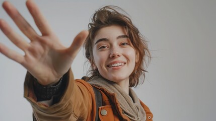 Positive optimistic woman taking selfie POV, flirting, expressing happiness, waving hand, saying hello, wearing casual style jacket. Indoor studio shot isolated on gray background.