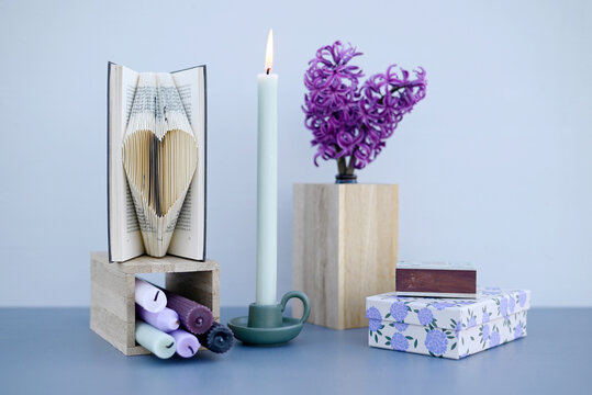 Studio shot of burning candle, blooming hyacinths and heart carved in book pages