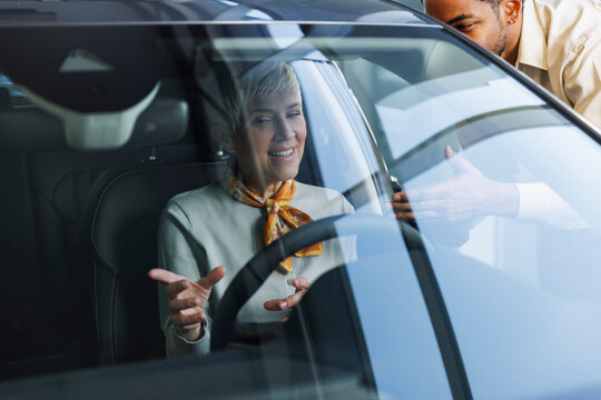 Salesperson with happy senior woman examining car in showroom