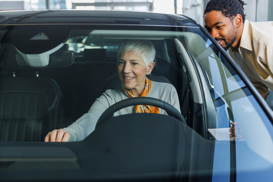 Smiling salesperson with woman examining car in showroom