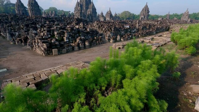 Revealing tilting up shot of Candi Sewu or Thousand Temple from showing green plant view with ancient temple and blue sky background