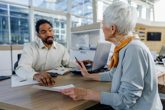 Senior woman holding contract and discussing with salesperson at desk