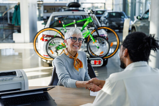 Happy senior woman shaking hands with salesperson at desk