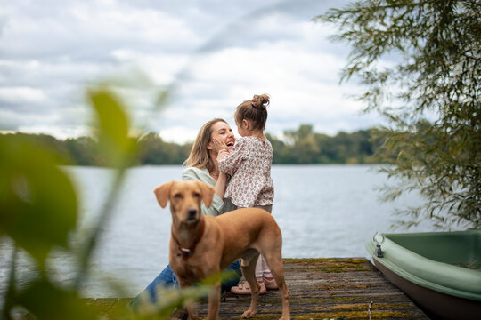 Happy woman having fun with daughter near dog in front of lake