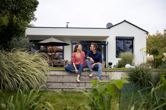 Smiling couple looking at each other in front of house