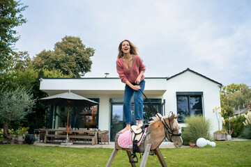 Cheerful woman standing on wooden horse in front of house