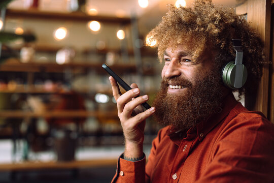Smiling businessman wearing wireless headphones listening to music and holding smart phone