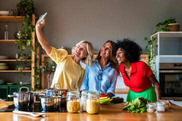 Smiling friends taking selfie on smart phone in kitchen at home
