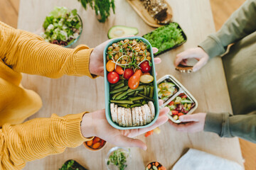 Hands of woman holding vegetarian food lunch box near man at table