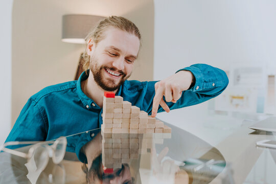 Happy businessman playing on steps made of wooden toy blocks at desk in office