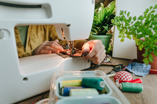 Man sewing recycled clothes through machine at home