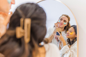 Smiling couple doing skincare and taking picture in front of mirror at home