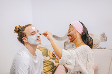 Happy woman applying skincare mask on boyfriend's face at home