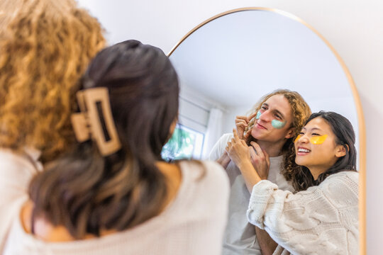 Happy couple applying skincare patches under eyes in front of mirror at home - Powered by Adobe