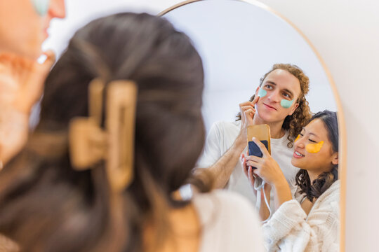 Smiling couple doing skincare and taking picture in front of mirror at home
