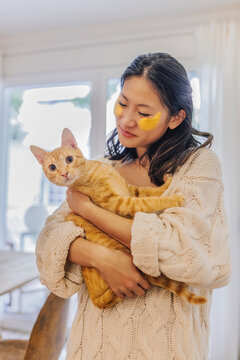 Smiling woman with under eye patches holding cat at home