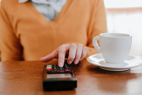Woman entering pin on credit card reader near coffee cup at table