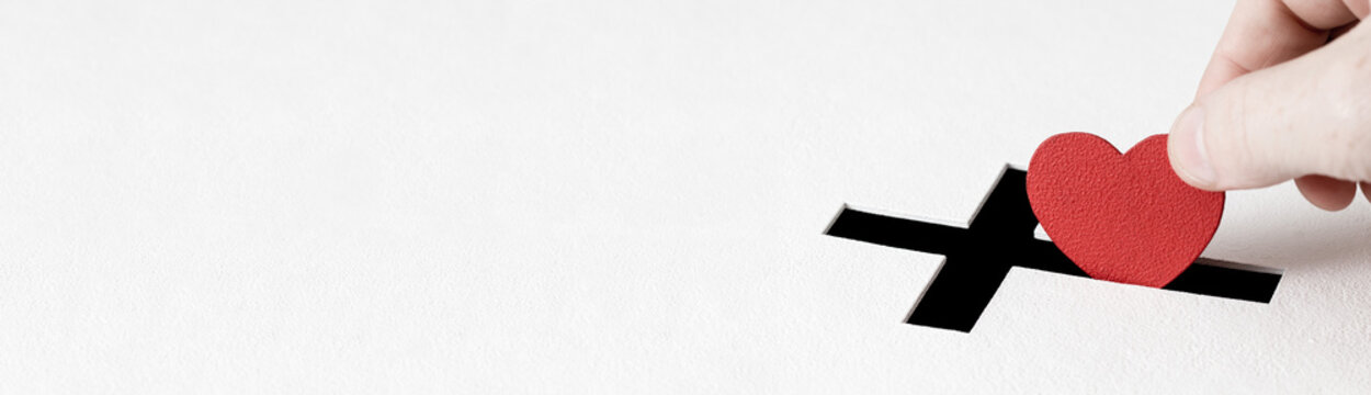 Concept of donation. Red heart symbol is put by person's hand into slot of donation box. Banner with copy space