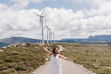 Spain, Madrid, Pregnant woman standing with raised arms in middle of road stretching past wind farm
