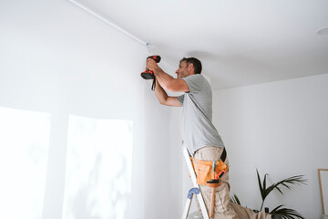 Repairman drilling hole in wall at home