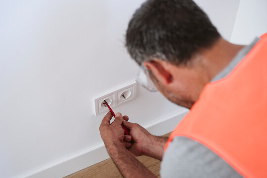 Mature technician repairing electrical outlet at home