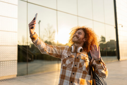 Happy man waving on video call through smart phone near building
