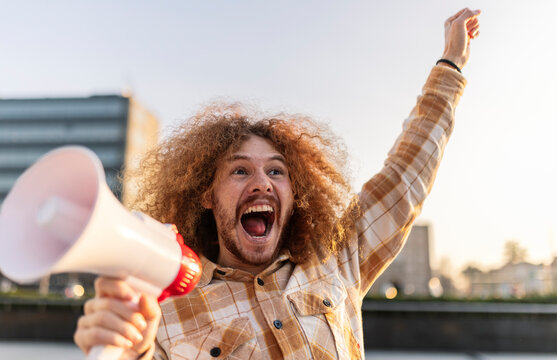 Cheerful man shouting with megaphone under sky