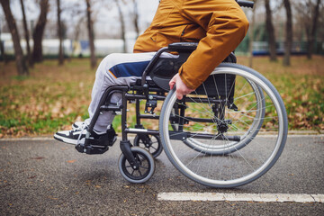 Close up image of paraplegic handicapped man in wheelchair in park. He is rolling on pathway. - obrazy, fototapety, plakaty
