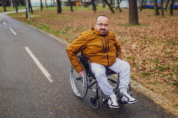 Fototapeta premium Portrait of happy paraplegic handicapped man in wheelchair in park. He is rolling on pathway.