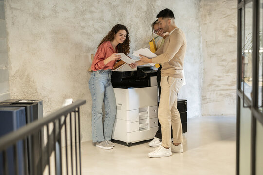 Young business colleagues discussing over documents standing by photocopier at office