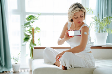 Woman with diabetes measuring blood sugar level through smart phone app at home