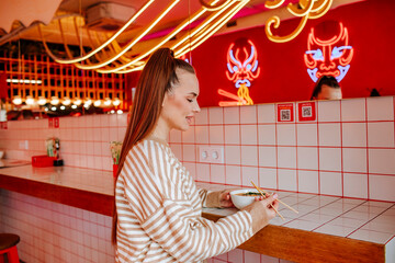 Smiling woman eating ramen noodles on tile table at restaurant