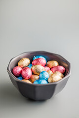 Easter chocolate eggs wrapped in aluminium foil in bowl on gray background.