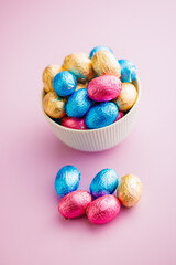 Easter chocolate eggs wrapped in aluminium foil in bowl on pink background.