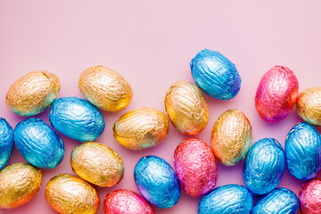 Easter chocolate eggs wrapped in aluminium foil on pink background. Top view.
