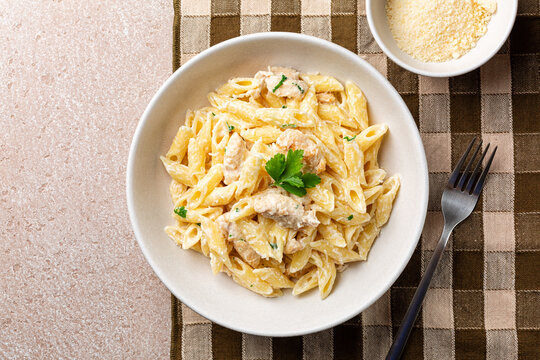 Chicken Alfredo penne, creamy pasta wich parmesan cheese in a white plate on a brown napkin. Directly above. - Powered by Adobe